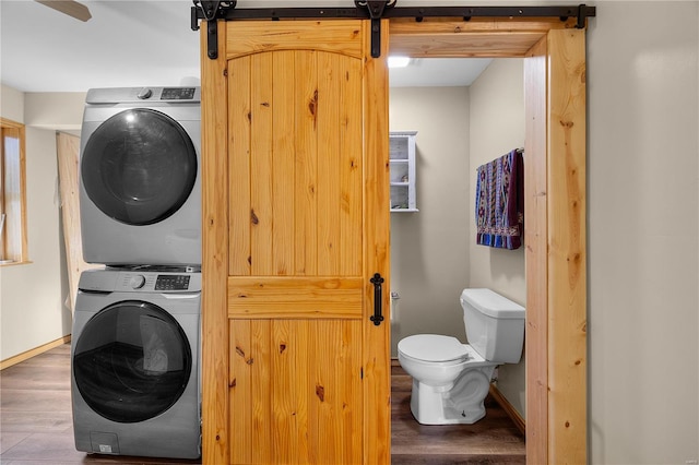 washroom featuring dark wood-type flooring, stacked washer / drying machine, and a barn door