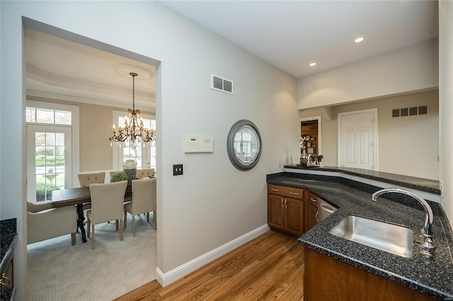 bar featuring dark stone counters, sink, decorative light fixtures, light wood-type flooring, and a notable chandelier