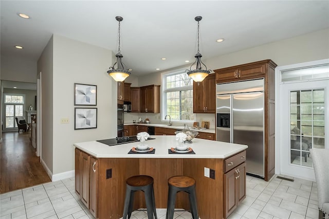 kitchen with a breakfast bar, built in fridge, hanging light fixtures, black electric cooktop, and a kitchen island