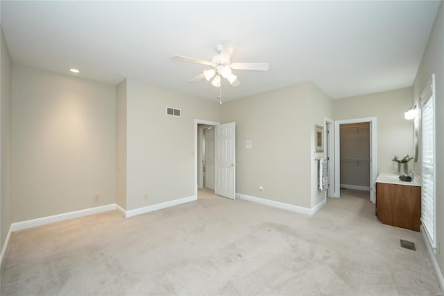 unfurnished bedroom with a walk in closet, ceiling fan, a closet, and light carpet