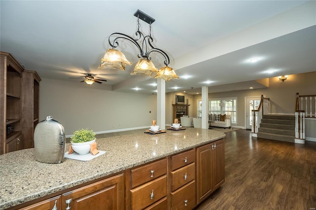 kitchen featuring dark hardwood / wood-style flooring, ceiling fan, light stone counters, and hanging light fixtures