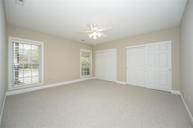 unfurnished bedroom with multiple closets, ceiling fan, and light colored carpet