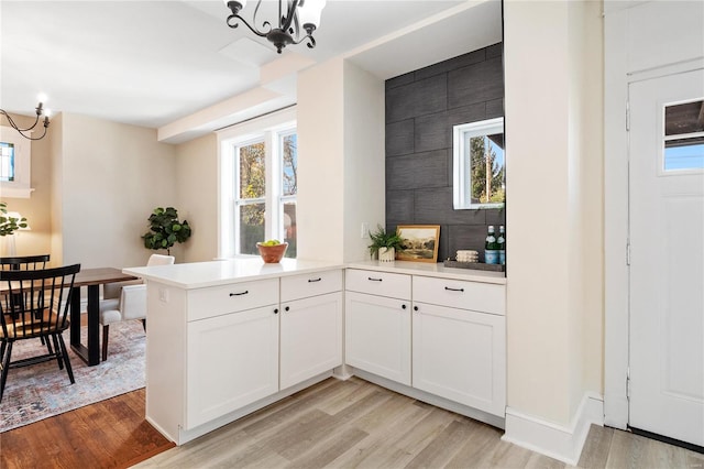 kitchen with white cabinetry, kitchen peninsula, a chandelier, and light hardwood / wood-style flooring