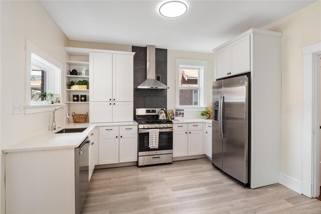 kitchen featuring wall chimney exhaust hood, sink, light wood-type flooring, appliances with stainless steel finishes, and white cabinets