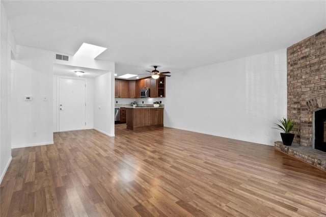 unfurnished living room with a fireplace, light wood-type flooring, a skylight, and ceiling fan