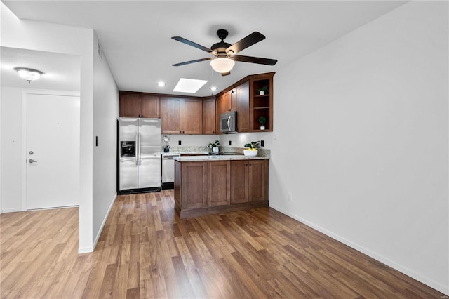 kitchen featuring a skylight, ceiling fan, stainless steel appliances, kitchen peninsula, and light wood-type flooring