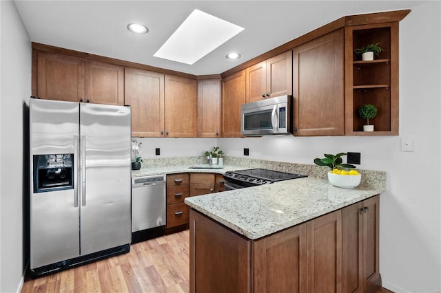 kitchen with light hardwood / wood-style flooring, a skylight, light stone countertops, kitchen peninsula, and stainless steel appliances