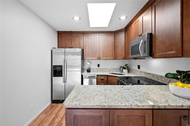 kitchen with appliances with stainless steel finishes, a skylight, light stone counters, sink, and light hardwood / wood-style flooring