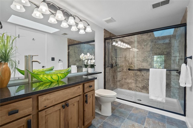 bathroom with vanity, a skylight, toilet, and a shower with shower door