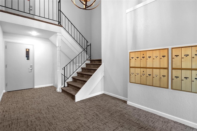 carpeted foyer entrance with a towering ceiling, a mail area, and a notable chandelier