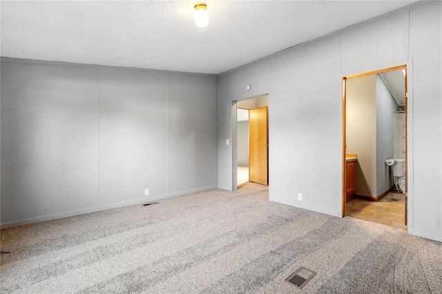 unfurnished bedroom with a textured ceiling, ensuite bathroom, and light colored carpet