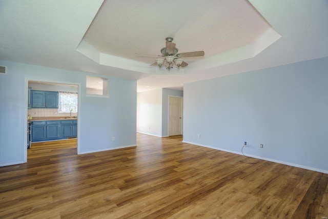 spare room featuring a tray ceiling, ceiling fan, dark hardwood / wood-style flooring, and sink