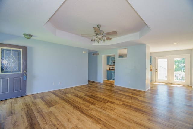 unfurnished living room with a tray ceiling, ceiling fan, and light hardwood / wood-style flooring