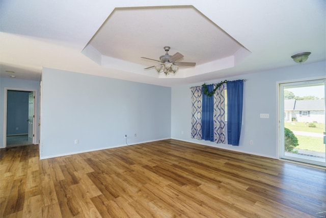 empty room with a tray ceiling, ceiling fan, and wood-type flooring