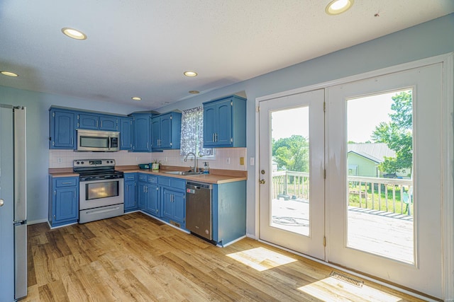 kitchen featuring sink, blue cabinetry, appliances with stainless steel finishes, light hardwood / wood-style floors, and backsplash