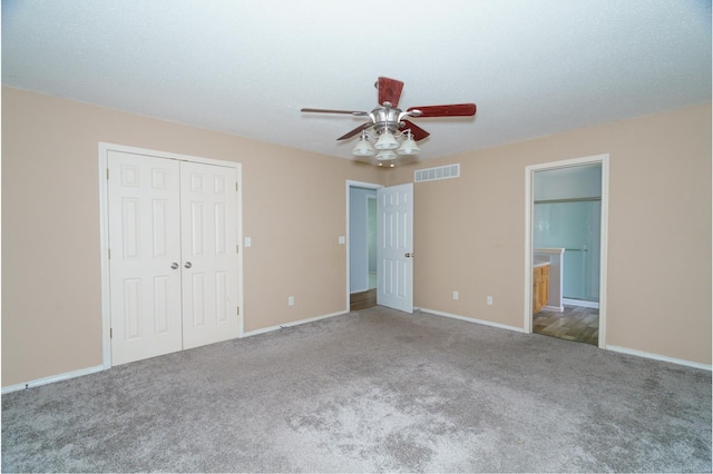 unfurnished bedroom with carpet, a closet, ensuite bathroom, and ceiling fan