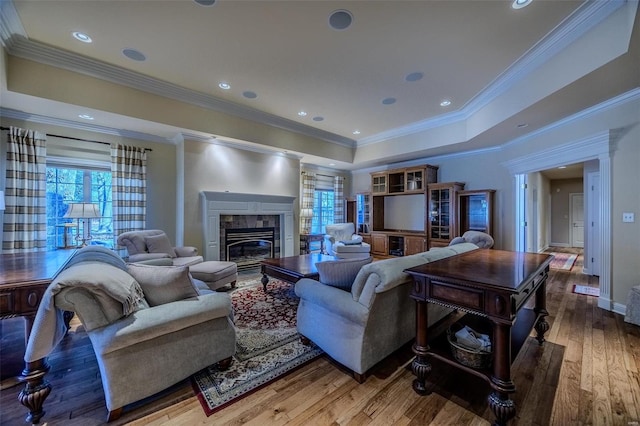 living room featuring hardwood / wood-style floors, ornamental molding, a tile fireplace, and a tray ceiling