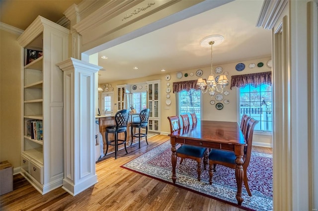 dining room featuring light wood-type flooring, crown molding, a notable chandelier, and ornate columns