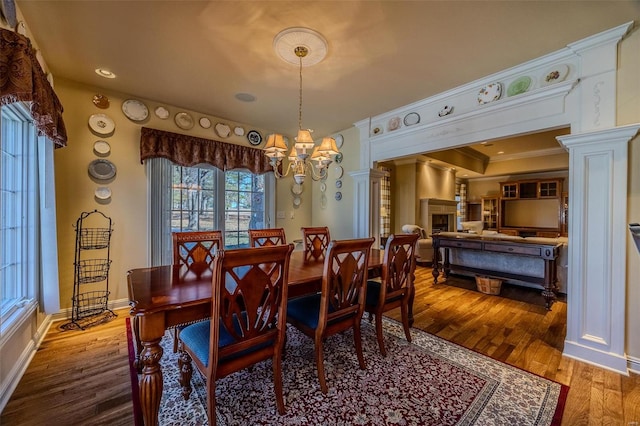 dining room with ornate columns, ornamental molding, a notable chandelier, and hardwood / wood-style flooring