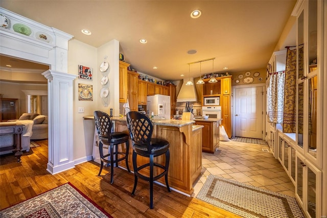 kitchen featuring kitchen peninsula, crown molding, white appliances, a breakfast bar area, and light wood-type flooring