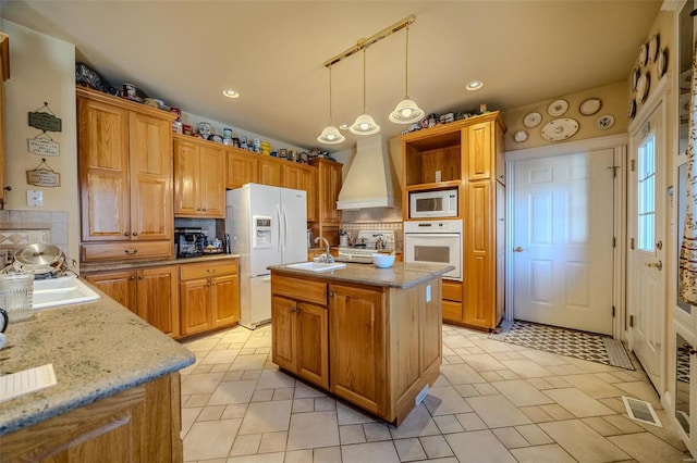 kitchen with backsplash, white appliances, a kitchen island with sink, and hanging light fixtures