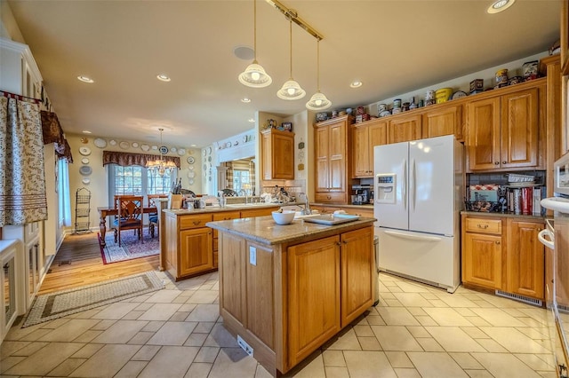 kitchen with hanging light fixtures, a center island with sink, kitchen peninsula, and white fridge with ice dispenser