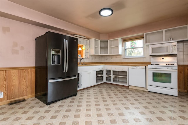 kitchen featuring backsplash, white appliances, sink, white cabinets, and wood walls