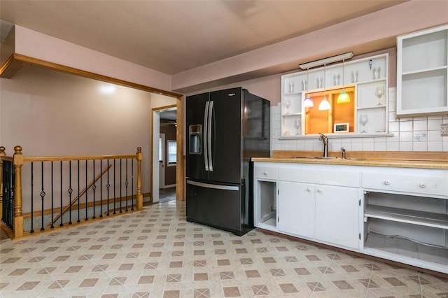 kitchen featuring decorative backsplash, black fridge, sink, and white cabinets