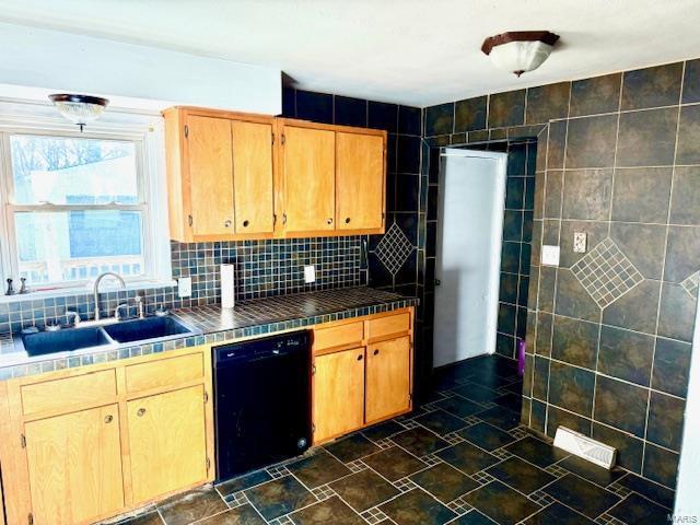 kitchen with tile countertops, black dishwasher, tasteful backsplash, tile walls, and sink