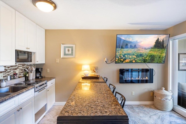 kitchen with tasteful backsplash, light tile patterned floors, dark stone countertops, white cabinets, and stainless steel range with gas cooktop