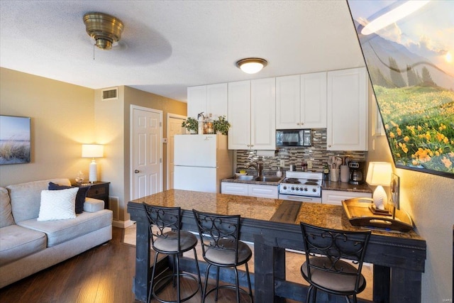 kitchen featuring decorative backsplash, white appliances, ceiling fan, dark wood-type flooring, and white cabinets