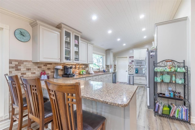 kitchen featuring kitchen peninsula, a kitchen breakfast bar, light stone counters, and lofted ceiling