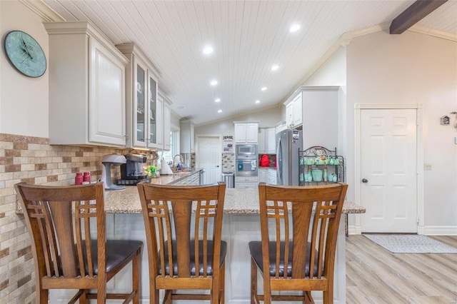 kitchen with vaulted ceiling with beams, tasteful backsplash, kitchen peninsula, light wood-type flooring, and stainless steel appliances