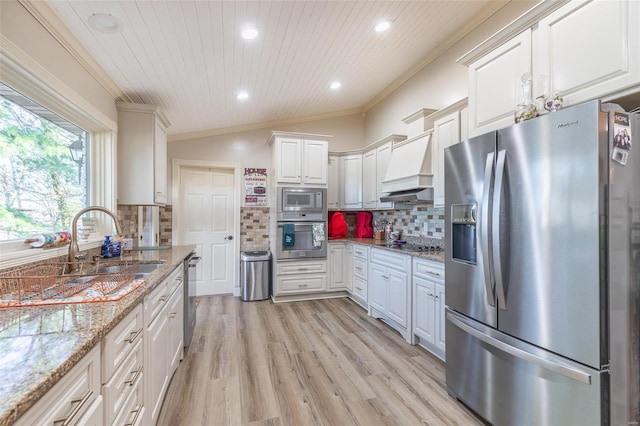 kitchen with decorative backsplash, appliances with stainless steel finishes, premium range hood, vaulted ceiling, and white cabinetry