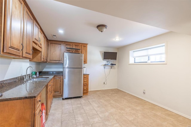 kitchen featuring stainless steel refrigerator, sink, and dark stone countertops