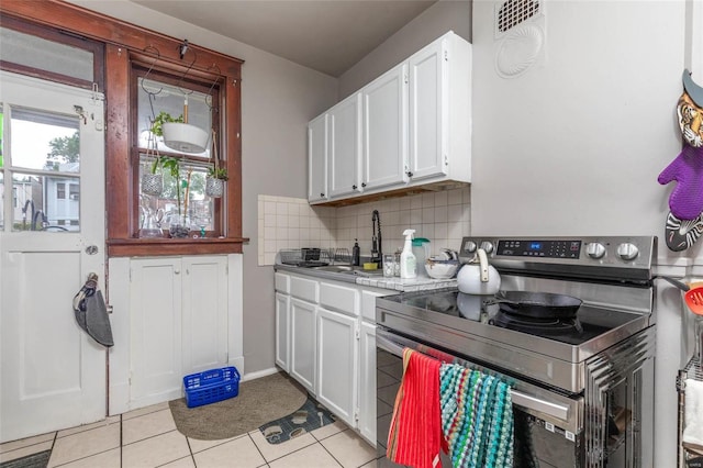 kitchen featuring backsplash, electric stove, sink, light tile patterned flooring, and white cabinetry