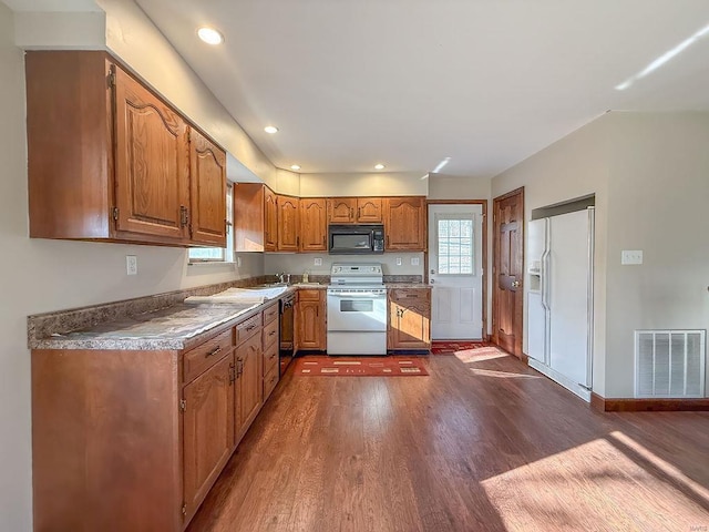 kitchen featuring visible vents, white appliances, brown cabinets, and dark wood-style floors