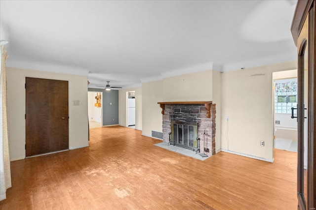 unfurnished living room featuring a stone fireplace, ceiling fan, and hardwood / wood-style floors