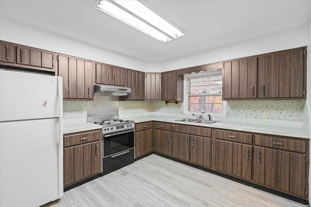 kitchen with dark brown cabinetry, gas stove, sink, white refrigerator, and light hardwood / wood-style flooring