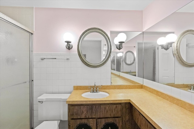 bathroom with vanity, toilet, a shower with door, and tile walls