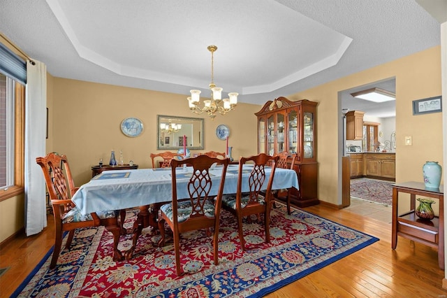 dining room featuring a notable chandelier, light hardwood / wood-style floors, a textured ceiling, and a tray ceiling