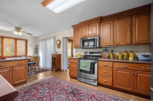 kitchen featuring light tile patterned floors, a textured ceiling, stainless steel appliances, and ceiling fan