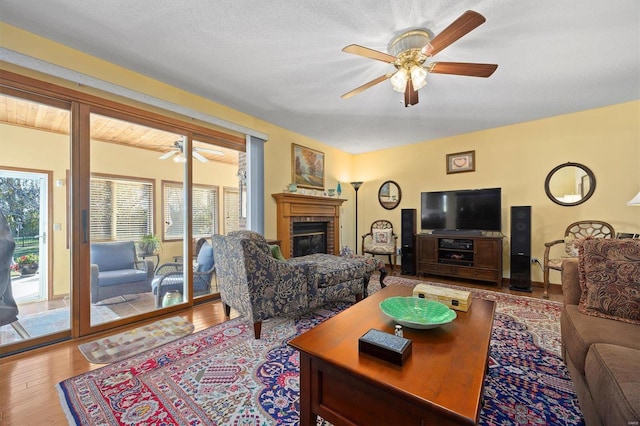 living room featuring hardwood / wood-style floors, a textured ceiling, a brick fireplace, and ceiling fan