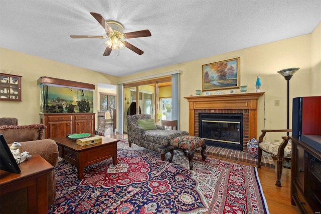 living room featuring hardwood / wood-style flooring, ceiling fan, a textured ceiling, and a brick fireplace