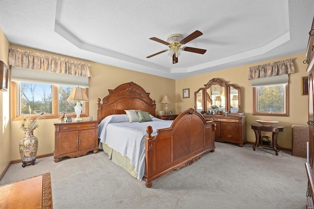 carpeted bedroom with a textured ceiling, a raised ceiling, and ceiling fan