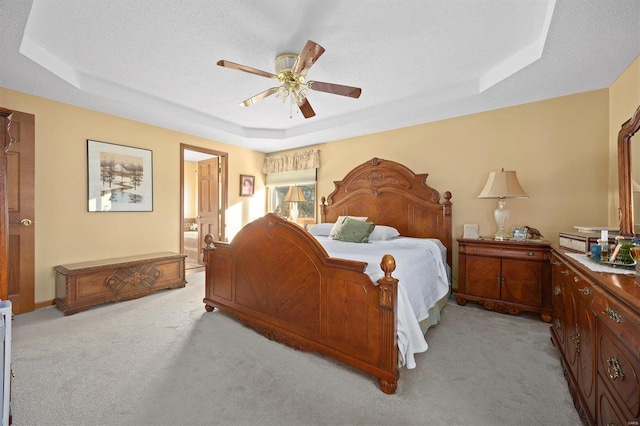 bedroom featuring light carpet, ensuite bathroom, a raised ceiling, and ceiling fan