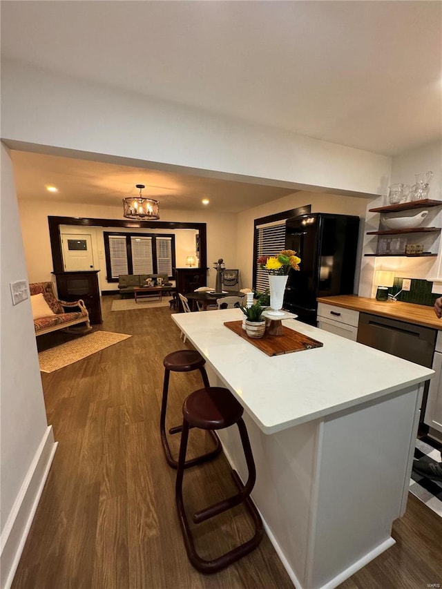 kitchen with black fridge, dark hardwood / wood-style floors, a chandelier, a breakfast bar, and a kitchen island