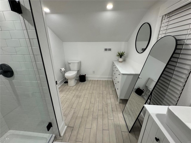 bathroom with a tile shower, vanity, lofted ceiling, and toilet