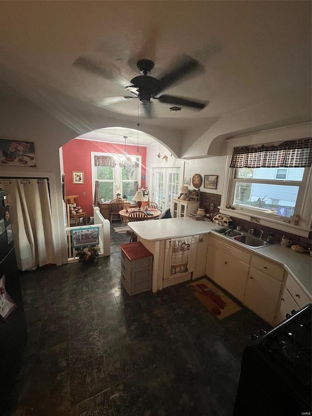 kitchen featuring black range oven, ceiling fan with notable chandelier, sink, vaulted ceiling, and kitchen peninsula