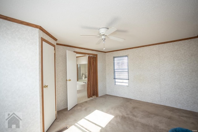 unfurnished bedroom with ensuite bath, ceiling fan, ornamental molding, a textured ceiling, and light colored carpet